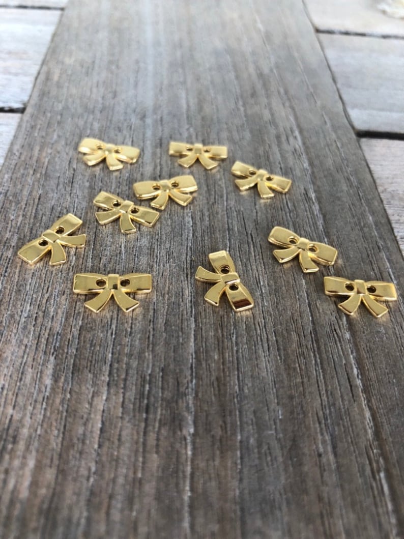 May include: Ten gold-colored metal bow-shaped buttons. The buttons have two holes each.