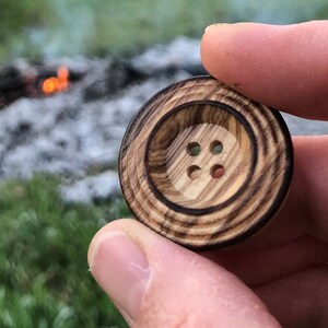 May include: A wooden button with a dark brown wood grain and four holes. The button has a concentric circle design.