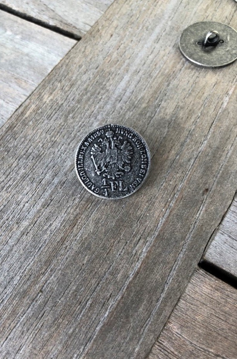 May include: A silver-toned button with a raised design of a double-headed eagle and the text "1 FL" in the center.