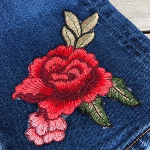 May include: A pair of blue denim shorts with a red embroidered rose and green leaves.