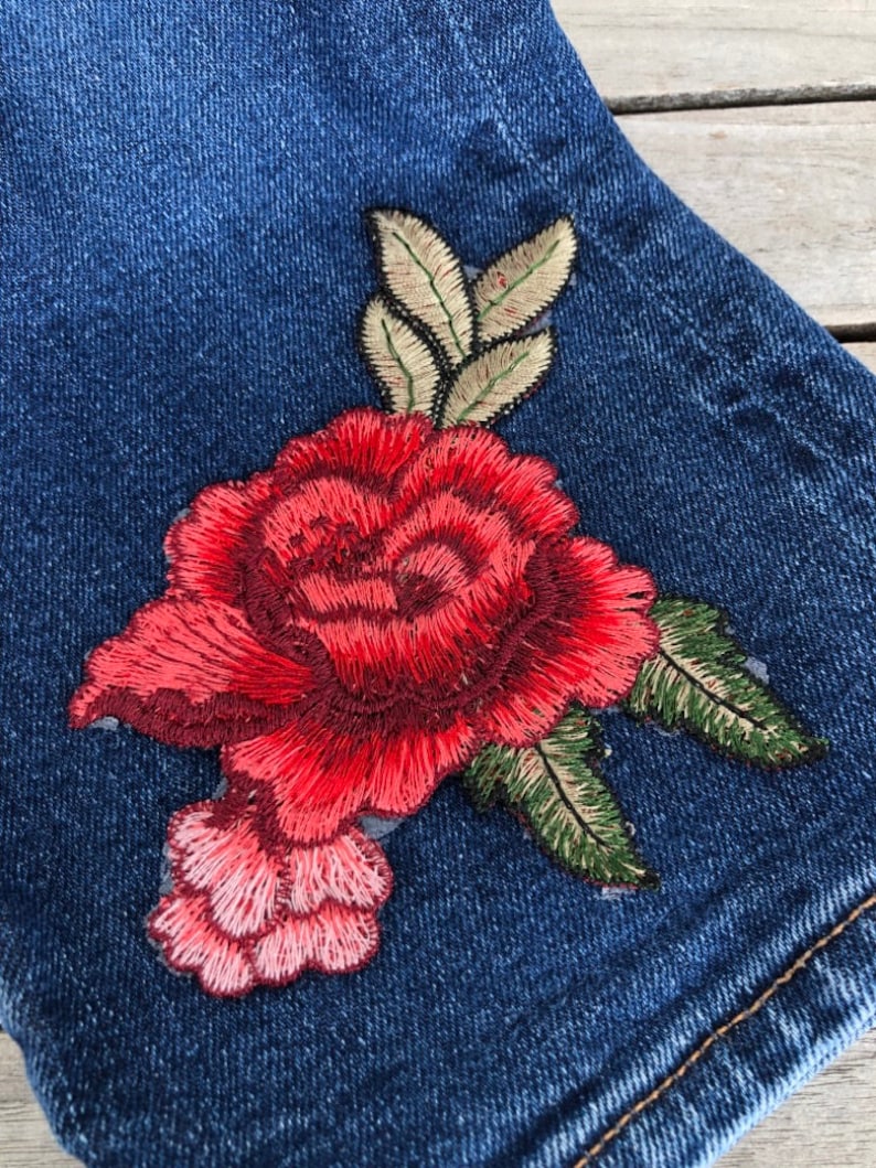 May include: A pair of blue denim shorts with a red embroidered rose and green leaves.