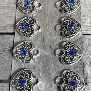 May include: Eight silver heart-shaped charms with blue rhinestone accents. Each charm has a loop for attaching to a bracelet or necklace.