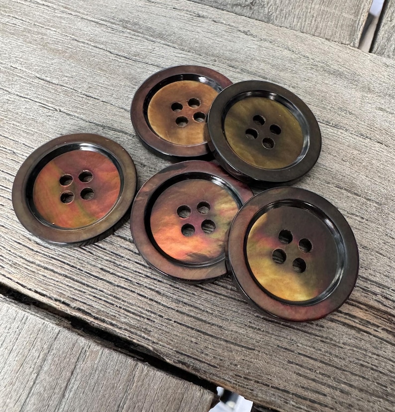 May include: A collection of five large, round buttons with a dark brown outer rim and a central section that shifts in color from gold to orange. Each button has four holes for sewing.