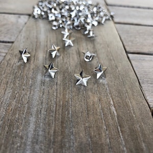 Könnte beinhalten: Ein Haufen silberner, sternförmiger Metallnieten, einige sind auf einer Holzoberfläche verstreut.