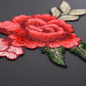 May include: Red embroidered rose with green leaves, a floral applique patch for sewing or crafting.