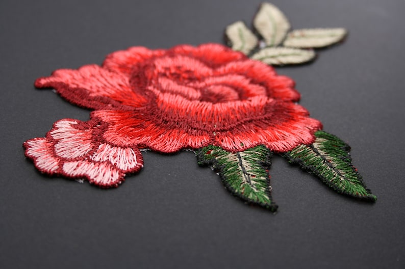 May include: Red embroidered rose with green leaves, a floral applique patch for sewing or crafting.
