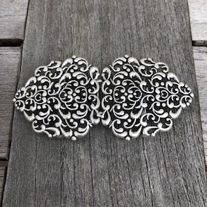 Op de afbeelding: Een zilveren filigrein gesp met een decoratief bloemmotief.