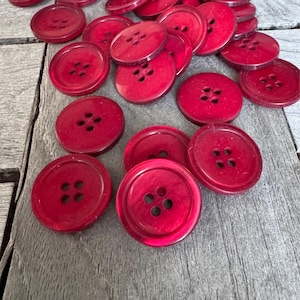 Op de afbeelding: Een stapel rode plastic knopen met elk vier gaten. De knopen zijn willekeurig gerangschikt op een houten oppervlak.