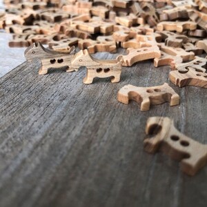Peut inclure: Un tas de boutons en bois en forme de chien dans diff&eacute;rentes nuances de brun. Deux boutons sont au premier plan, l'un face &agrave; l'appareil photo et l'autre face &agrave; droite.