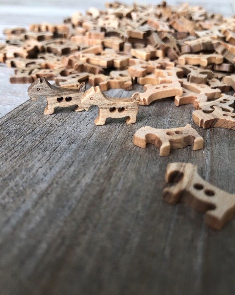 Peut inclure: Un tas de boutons en bois en forme de chien dans diff&eacute;rentes nuances de brun. Deux boutons sont au premier plan, l'un face &agrave; l'appareil photo et l'autre face &agrave; droite.