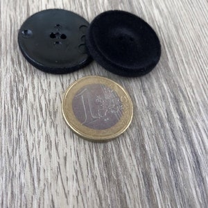 May include: Two black buttons, one with a smooth surface and the other with a textured surface, are shown next to a euro coin.