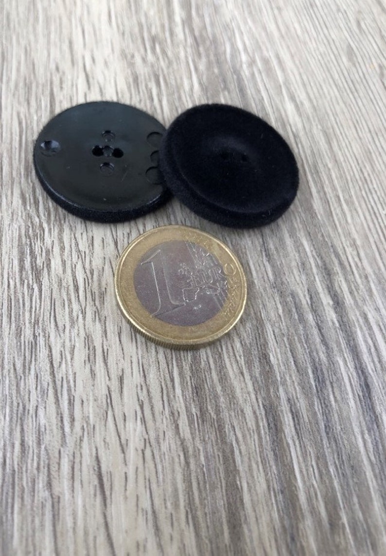 May include: Two black buttons, one with a smooth surface and the other with a textured surface, are shown next to a euro coin.