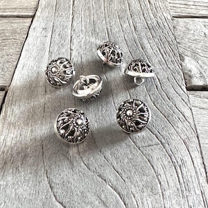 Könnte beinhalten: Sechs silberne Metallknöpfe mit einem komplizierten floralen Design. Die Knöpfe sind rund und haben eine erhabene Mitte.