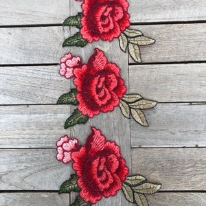 May include: Three red embroidered rose appliques with green leaves on a wood background.
