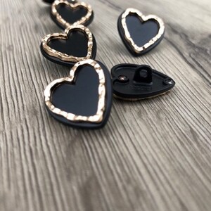 May include: A set of black heart-shaped buttons with a gold trim. The buttons have a shiny finish and are perfect for adding a touch of elegance to any project.