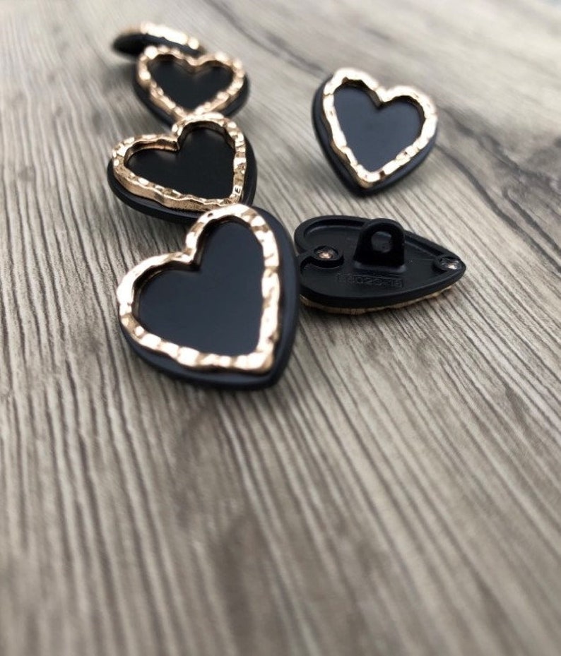 May include: A set of black heart-shaped buttons with a gold trim. The buttons have a shiny finish and are perfect for adding a touch of elegance to any project.