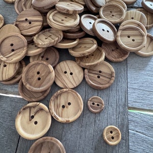 May include: A collection of wooden buttons in various sizes and shades of brown. The buttons have two holes each and are made from natural wood with a unique grain pattern.