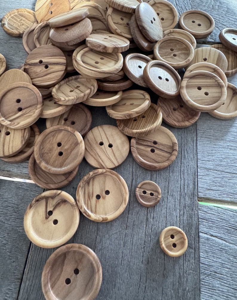 May include: A collection of wooden buttons in various sizes and shades of brown. The buttons have two holes each and are made from natural wood with a unique grain pattern.