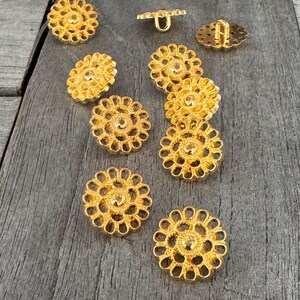 Puede incluir: Diez botones de metal de color dorado con un diseño floral circular decorativo. Los botones tienen un centro elevado y un agujero para coser.