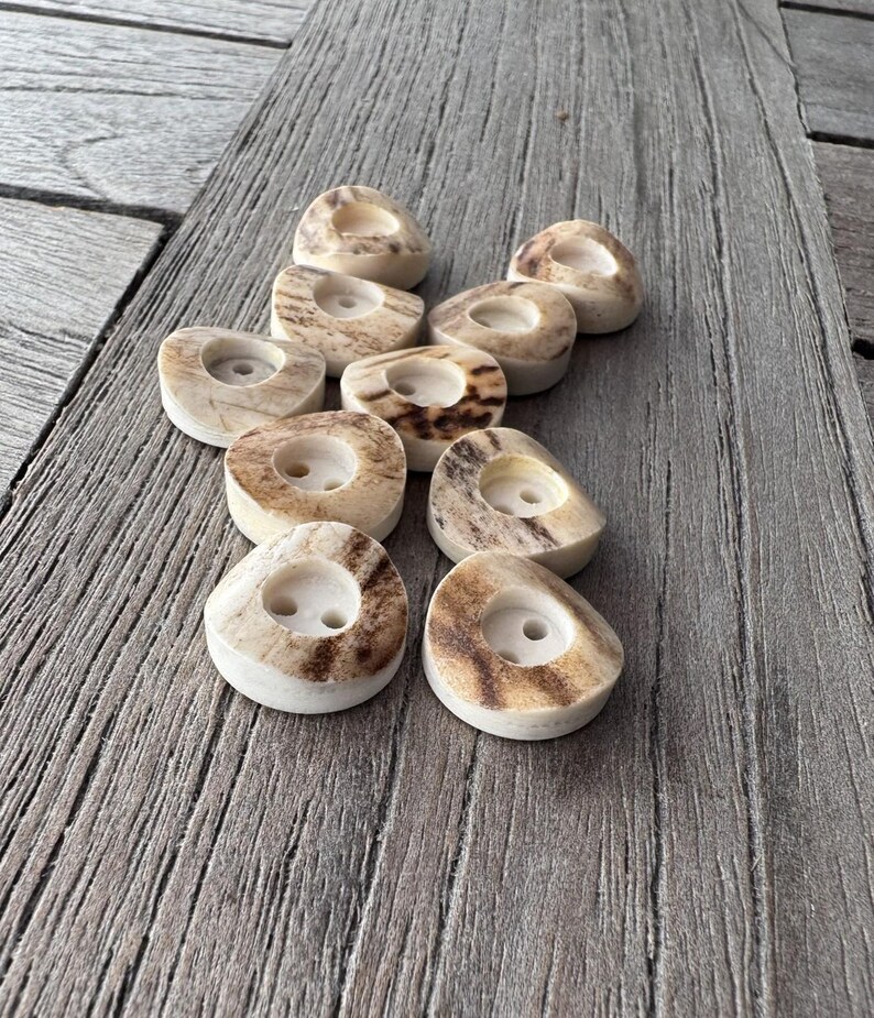May include: A collection of small, off-white candle holders with a natural, speckled brown pattern. Each holder has a circular indentation for a candle. The holders are arranged on a weathered wooden surface.