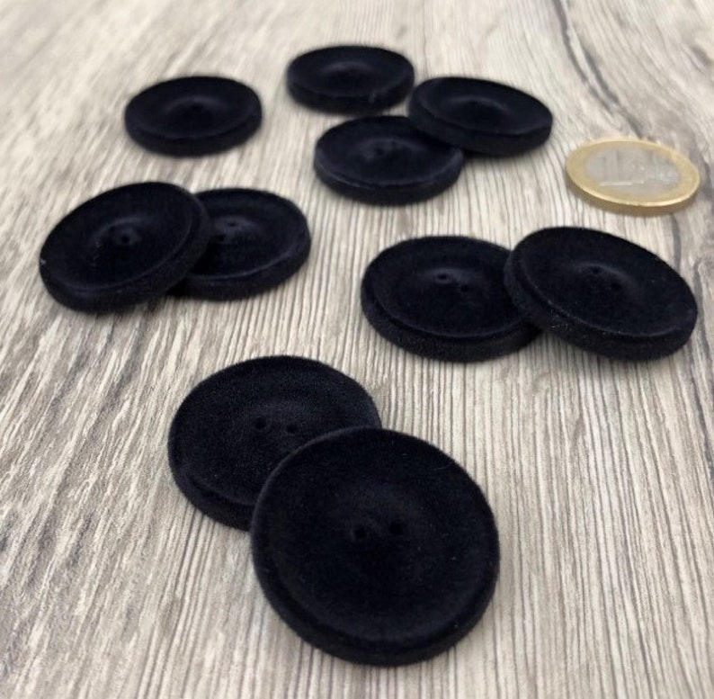 May include: Ten black velvet buttons with two holes each. The buttons are round and have a slightly raised center.