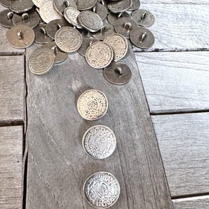 Könnte beinhalten: Nahaufnahme einer Reihe von silbernen Metallknöpfen mit komplizierten Designs. Die Knöpfe sind auf einer Holzoberfläche zu einem Stapel angeordnet.