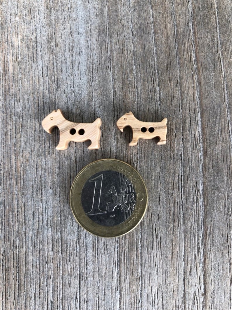Peut inclure: Deux boutons en bois en forme de chien. Les boutons sont bruns et ont deux trous chacun. Une pi&egrave;ce d'un euro est incluse pour r&eacute;f&eacute;rence de taille.