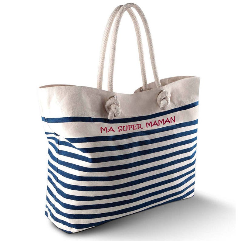 May include: A canvas tote bag with navy blue and white horizontal stripes. The bag has a white top with the red text "MA SUPER MAMAN". It features rope handles and is suitable for carrying items.