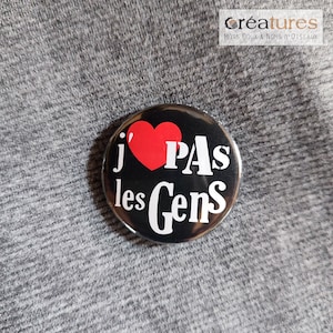 Puede incluir: Un botón negro y blanco con un corazón rojo y el texto "j' PAS les Gens".