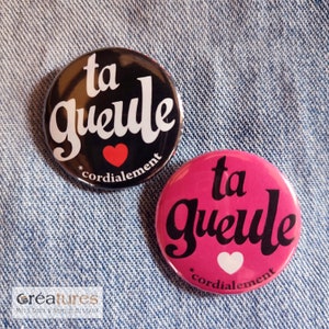 Peut inclure: Deux boutons ronds noirs et roses avec la phrase française "ta gueule" (ta gueule) en lettres blanches. Les deux boutons ont un petit cœur rouge avec le mot "cordialement" en dessous.