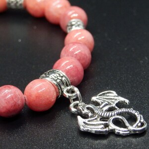 Pode incluir: Um bracelete de pedras cor-de-rosa com contas prateadas e um pingente de dragão prateado.