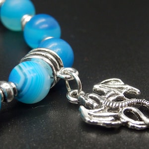 Pode incluir: Um bracelete de contas de ágata azul com um fecho de dragão prateado. As contas são uma mistura de azul sólido e azul com listras brancas.