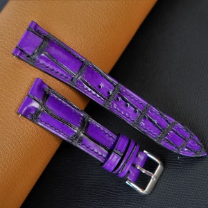 Puede incluir: Dos correas de reloj de cuero morado con un patr&oacute;n de cocodrilo. Las correas tienen costuras negras y se muestran sobre una superficie de cuero marr&oacute;n.