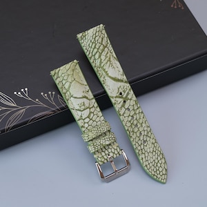 May include: A two-piece watch strap featuring a light green and white textured pattern resembling reptile skin. The strap includes a polished silver-tone metal buckle and two matching leather keepers, designed for attachment to a wristwatch case.