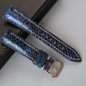 Puede incluir: Dos correas de reloj azules con estampado de piel de serpiente. Las correas tienen una hebilla plateada y están hechas de cuero.