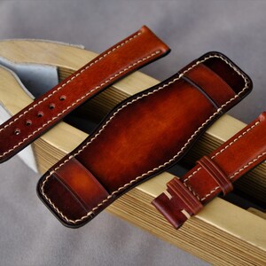 May include: Three brown leather watch straps with white stitching. The straps are displayed on a wooden surface.