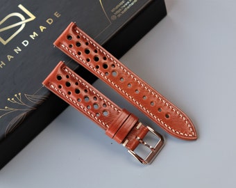 May include: Two brown leather watch straps with white stitching and holes. The straps are laid out on a black box with the word "HANDMADE" printed on it.
