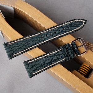 May include: Two dark green leather watch straps with white stitching. The straps are laid out on a wooden watch strap sizing tool.