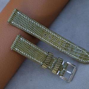 Könnte beinhalten: Zwei grüne Armbänder aus Leder mit Eidechsenprägung und weißen Nähten. Die Armbänder sind auf einer braunen Lederoberfläche abgebildet.