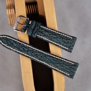 May include: Two dark green leather watch straps with white stitching. The straps are on a wooden surface.