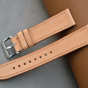 May include: Two light brown leather watch straps with white stitching. The strap on the left has a silver buckle. The strap on the right has five holes for adjusting the length.