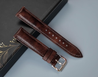May include: Two brown leather watch straps with white stitching. The straps are on a black background. One strap has a silver buckle.