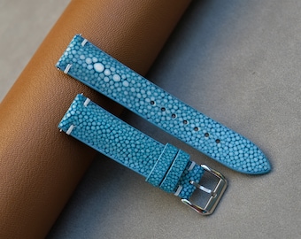 May include: Two light blue leather watch straps with a textured pattern. The straps are made of stingray skin and have white stitching.
