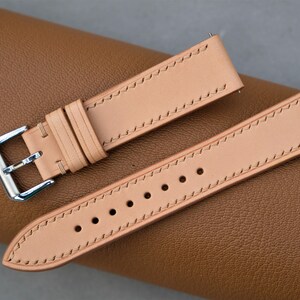 May include: Two light brown leather watch straps with stitching. One strap has a silver buckle.