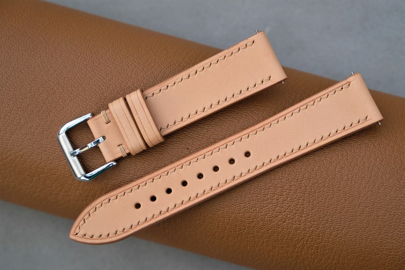 May include: Two light brown leather watch straps with stitching. One strap has a silver buckle.