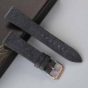 May include: Two gray leather watch straps with a textured surface. One strap has a gold buckle.