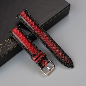 May include: Two red and black leather watch straps with a braided pattern. The straps are on a black box with gold floral designs.