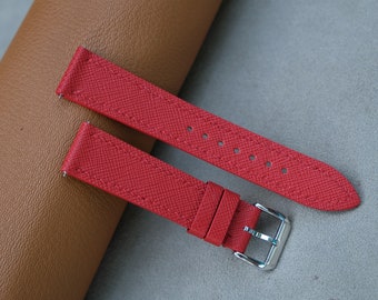 May include: Two red leather watch straps with a silver buckle. The straps have a textured surface and are laid out on a brown surface.