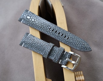 May include: Two gray leather watch straps with a textured pattern. The straps are on a wooden surface.