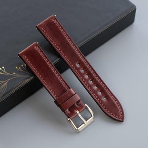 May include: Two brown leather watch straps with stitching detail. One strap has a silver buckle.